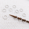 Set of 10 silver toned hexagon metal stitch markers for knitting shown on 4mm knitting needle.