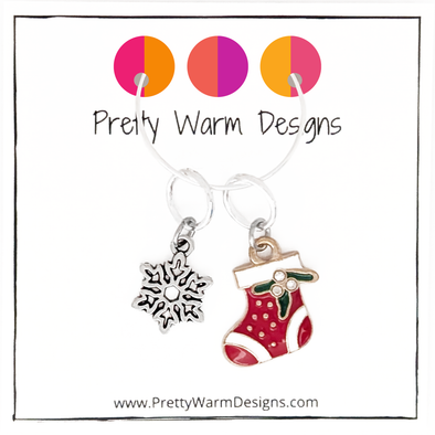 One red, white and green enamel with rhinestones Christmas stocking ring stitch marker and one silver alloy snowflake ring stitch marker for knitting with Pretty Warm Designs text and logo
