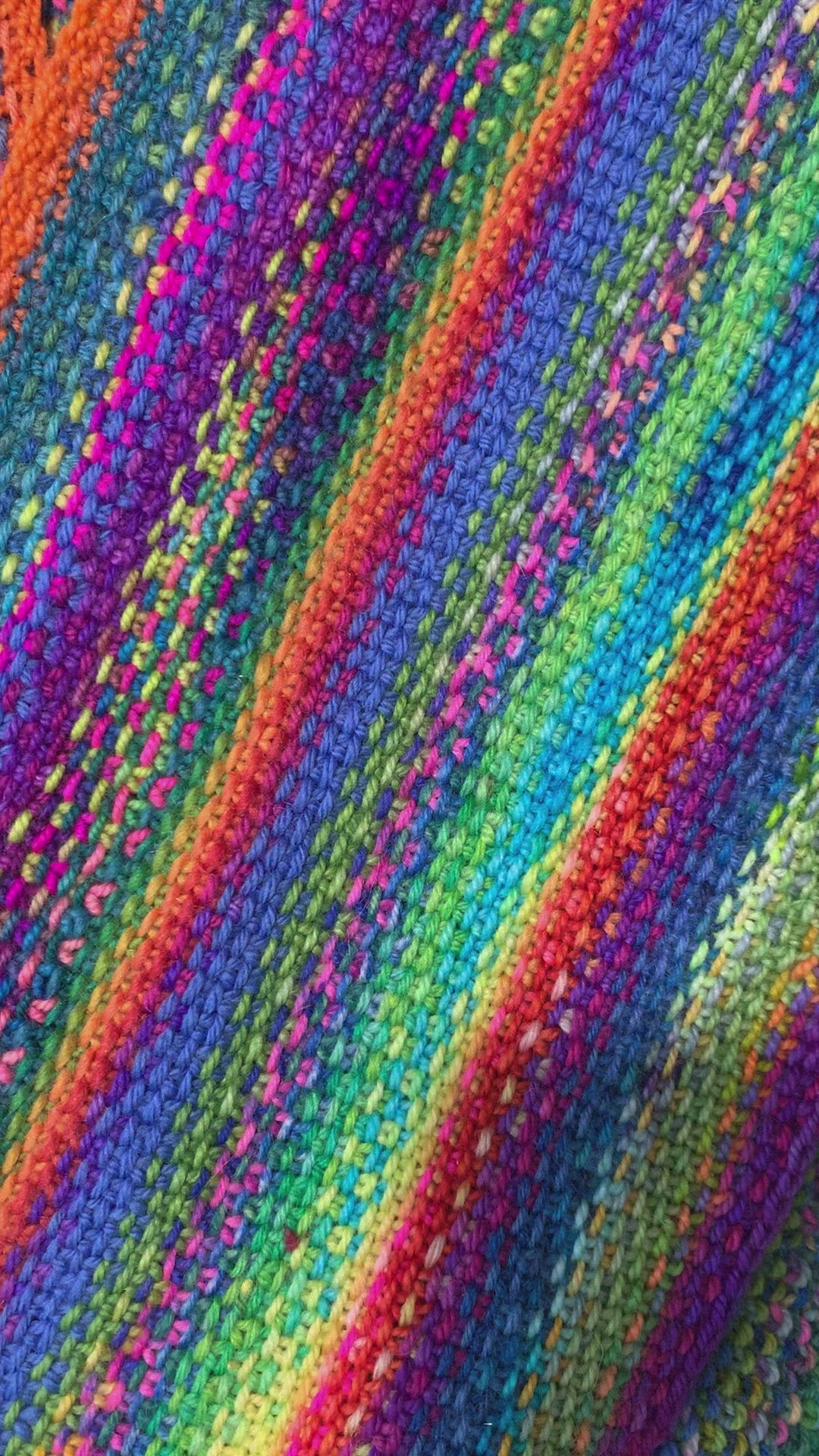 Video of six white, yellow and green enamel daisy charms snag free ring stitch markers held on knitting needle by woman's hand with multicoloured knitting in background by Pretty Warm Designs