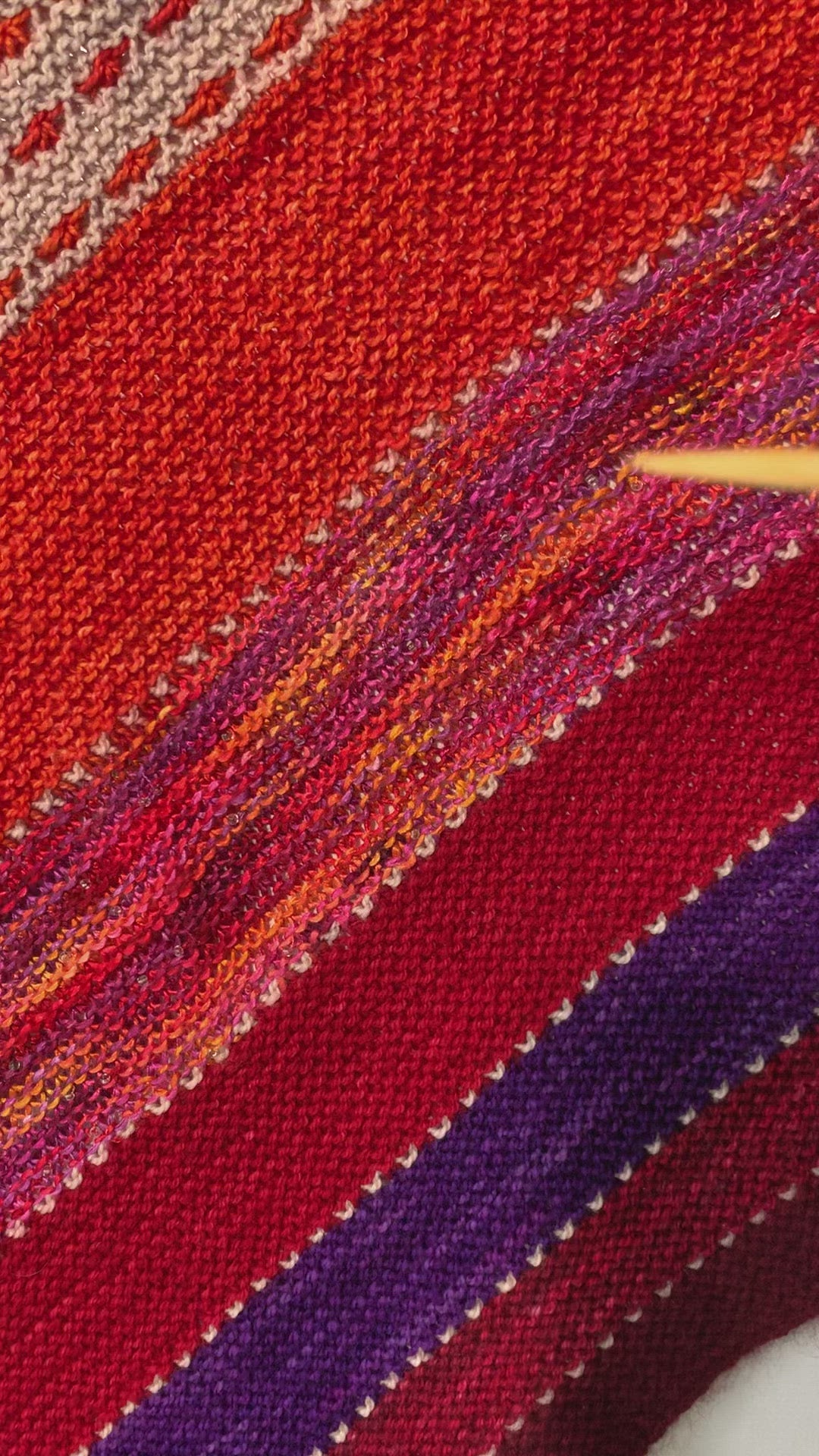 Video of six enamel butterfly charm snag free ring stitch markers in red, yellow, green, blue, pink and purple held on knitting needle in a woman's hand with an orange, red, purple and grey knitted shawl in the background by Pretty Warm Designs
