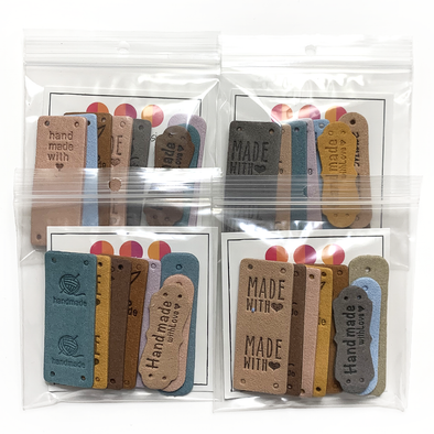 Four different packages of assorted PU vegan polyurethane leather garment label tags for knitted and crocheted projects packaged in clear poly zip bags sold by Pretty Warm Designs Inc.