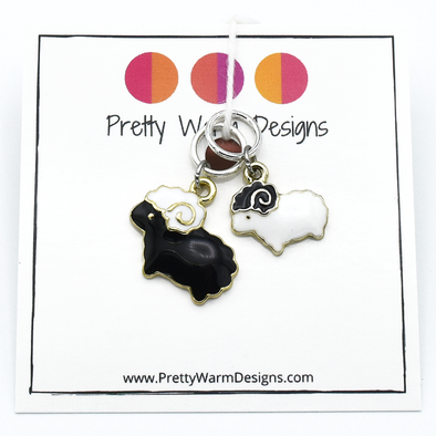 Package of two knitting stitch markers containing one black sheep and one white sheep ring marker attached to white cardstock with Pretty Warm Designs logo and text