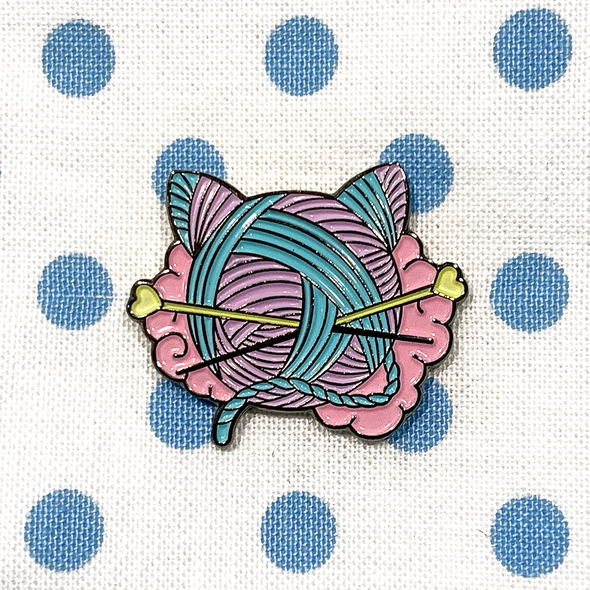 Pink, turquoise and yellow enamel on black background cat shaped yarn knitting pin on blue polka dot fabric bag by Pretty Warm Designs