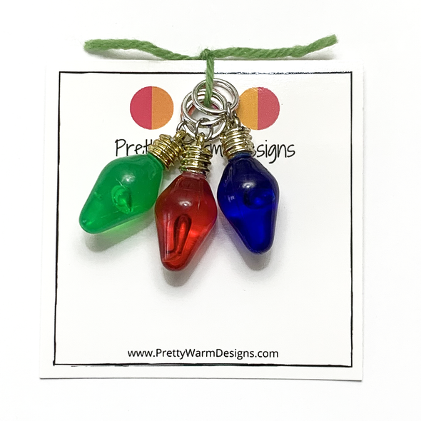 Set of 3 green, red and blue Christmas tree lights charm stitch marker for knitting tied with green yarn to cardstock with Pretty Warm Designs text and logo
