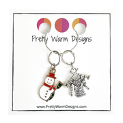 Two Winter-themed knitting ring stitch markers, one red, white and green enamel snowman and one antiqued Tibetan silver sweater on knitting needles attached with silver hoop ring to cardstock with Pretty Warm Designs text and logo
