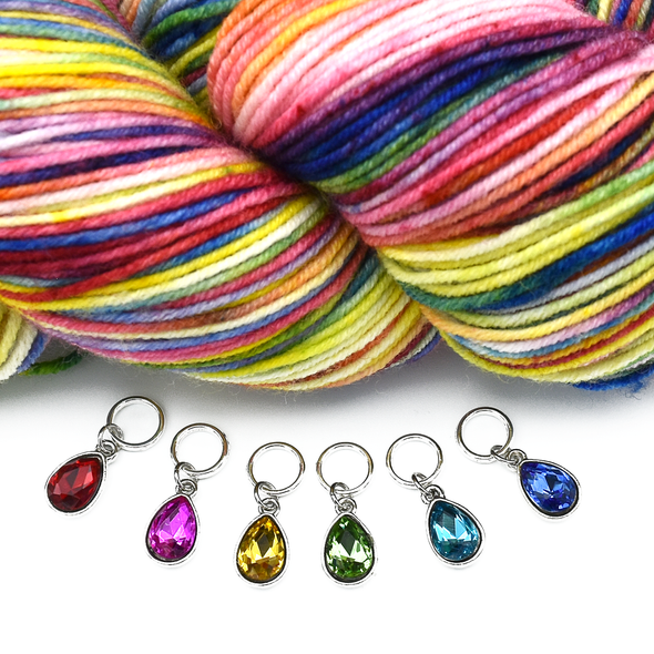 Set of six coloured rhinestones in red, pink, amber, green, turquoise and blue set in silver toned snag free ring stitch markers for knitting by Pretty Warm Designs and a variegated pink, blue, yellow, green, red and purple skein of yarn