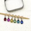 Set of six coloured rhinestones in red, pink, amber, green, turquoise and blue set in silver toned snag free ring stitch markers on a knitting needle and open decorative tin by Pretty Warm Designs