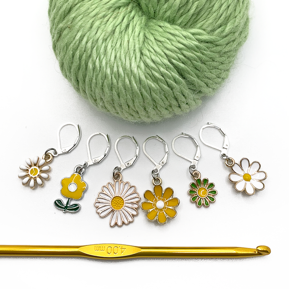 Set of six white, yellow and green enamel daisy charms with silver plated lever back clasps stitch markers for crochet with green yarn and gold crochet hook by Pretty Warm Designs