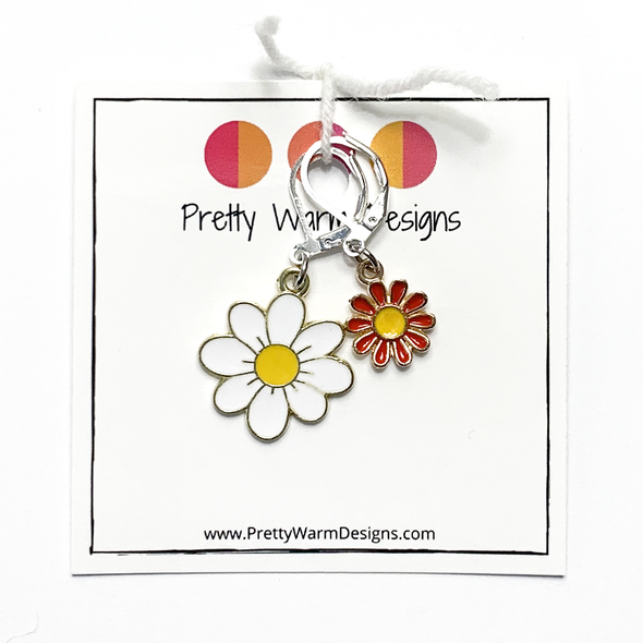 Two enamel charm crochet locking stitch markers with one white and one red daisy attached with white yarn to cardstock with Pretty Warm Designs text and logo