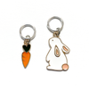 Two knitting ring stitch markers, one white and peach enamel bunny and one orange and green enamel carrot sold by Pretty Warm Designs Inc.