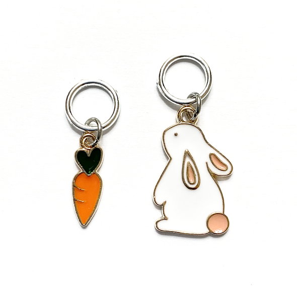 Two knitting ring stitch markers, one white and peach enamel bunny and one orange and green enamel carrot sold by Pretty Warm Designs Inc.