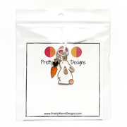 Two knitting ring stitch markers, one white and peach enamel bunny and one orange and green enamel carrot attached with white yarn to cardstock with Pretty Warm Designs text and logo packaged in a clear poly bag