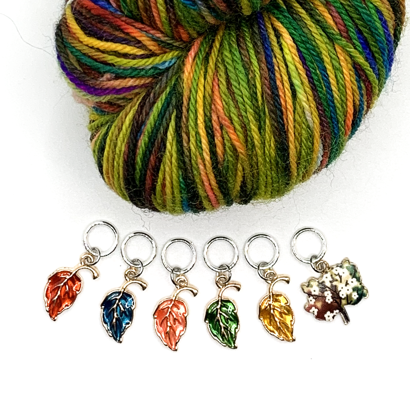 Set of five red, blue, orange, green and yellow enamel leaves and one tree charm snag free ring stitch markers with multicoloured yarn for knitting by Pretty Warm Designs