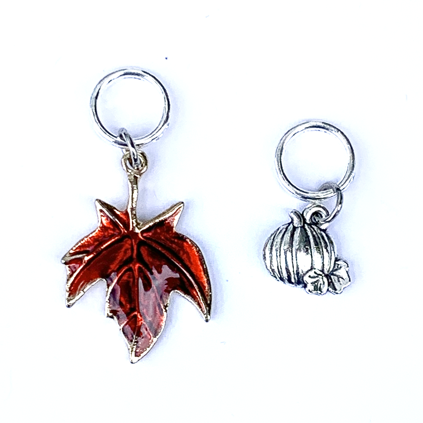 Two Fall-themed knitting ring stitch markers, one red enamel maple leaf and one silver toned pumpkin by Pretty Warm Designs