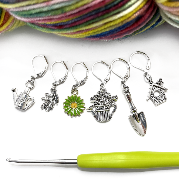 Set of one green and yellow enamel daisy and five antiqued silver alloy gardening themed locking stitch markers with a green handled crochet hook and multicoloured skein of yarn for crochet by Pretty Warm Designs Inc