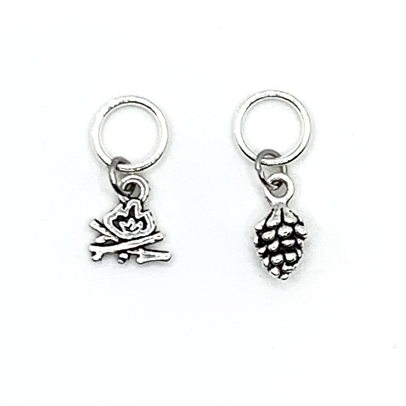 Two antiqued silver stitch markers, one camp fire and one pine cone for knitting by Pretty Warm Designs