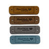 Four medium brown, dark brown, grey and teal coloured PU polyurethane vegan leather garment label tags for knitted and crocheted items sold by Pretty Warm Designs Inc.