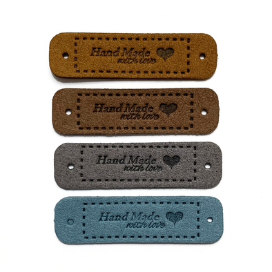 Four medium brown, dark brown, grey and teal coloured PU polyurethane vegan leather garment label tags for knitted and crocheted items sold by Pretty Warm Designs Inc.