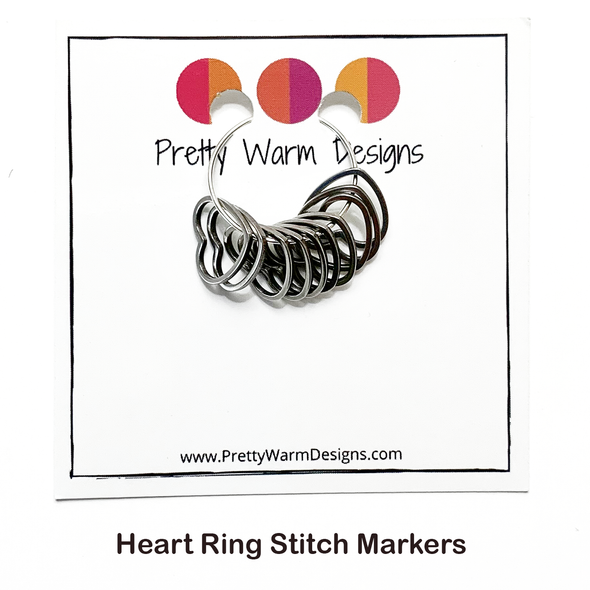 Set of ten silver coloured heart shaped ring stitch markers on a silver hoop attached to square white cardstock printed with the Pretty Warm Designs logo and URL for the Pacific Northwest Not Just Socks Yarn Box sold by Pretty Warm Designs Inc.