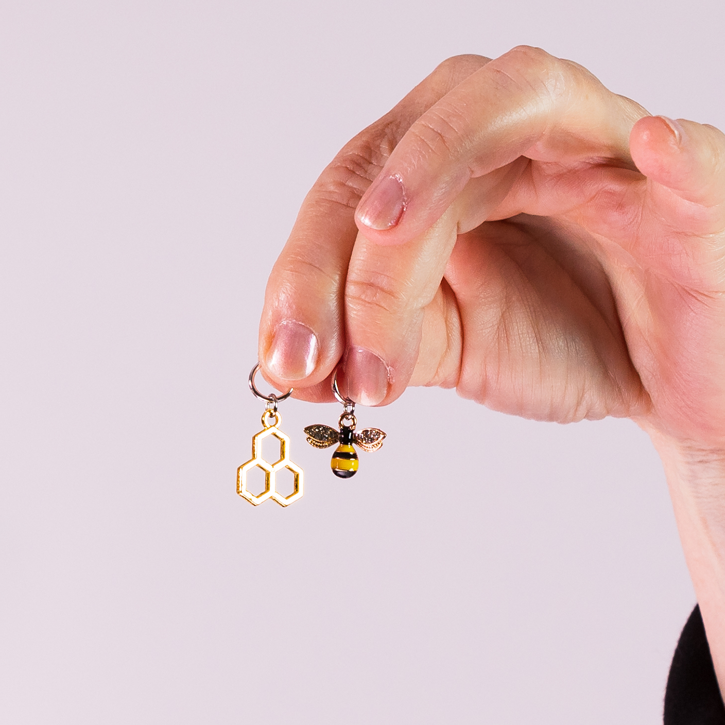 Hand holding honeycomb and bee stitch markers by Pretty Warm Designs