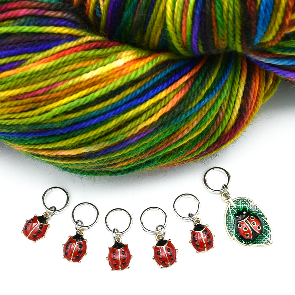 Set of five red and black enamel ladybug and one red, black and green ladybug on a leaf charms snag free ring stitch markers with a varietgated skein of yarn for knitting by Pretty Warm Designs