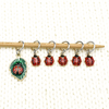 Set of five red and black enamel ladybug and one red, black and green ladybug on a leaf charms snag free ring stitch markers on a knitting needle resting on a white piece of knitting by Pretty Warm Designs