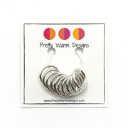 10 large ring silver plated stitch markers attached to card stock with Pretty Warm Designs logo and text