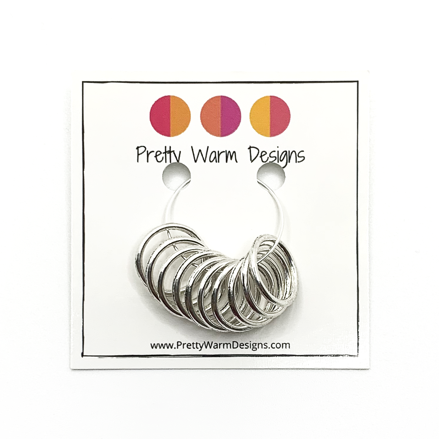 10 large ring silver plated stitch markers attached to card stock with Pretty Warm Designs logo and text