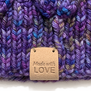 Tan PU polyurethane leather Made With Love garment label tag sewn onto purple lace knitted hat, sold by Pretty Warm Designs Inc.