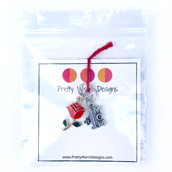 Two Mother's Day-themed knitting ring stitch markers, one red and green enamel rose and one silver #1 Mom attached with yarn to cardstock with Pretty Warm Designs text and logo in poly bag