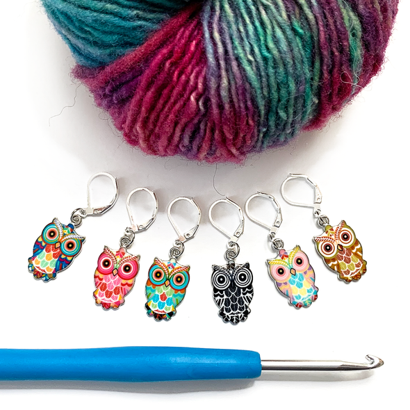 Set of six multicoloured enamel on silver toned alloy owl locking stitch markers with blue handled crochet hook and variegated green, red and purple yarn for crochet by Pretty Warm Designs