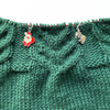 Two Christmas themed enamel stitch markers for knitting threaded on knitting needle cable and laying on green knitting sold by Pretty Warm Designs Inc