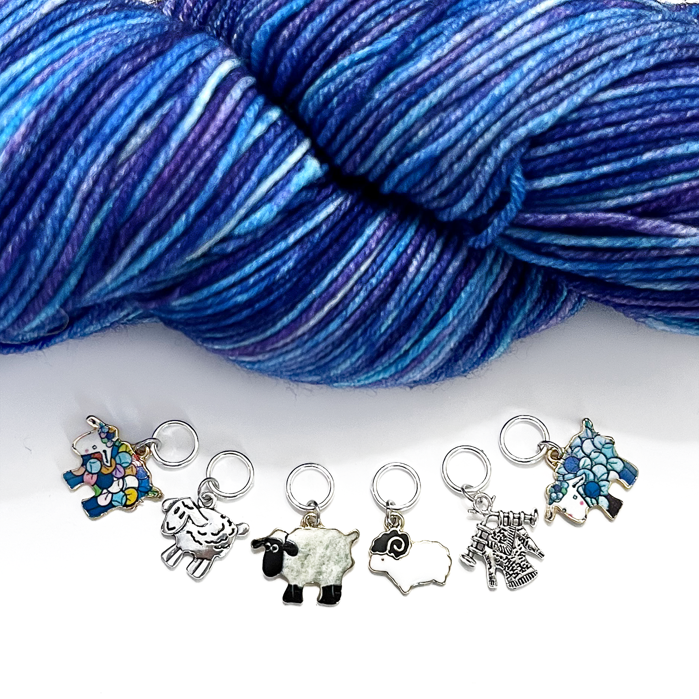 "Six sheep stitch markers displayed with blue variegated yarn — ring style knitting markers with enamel and silver sheep charms