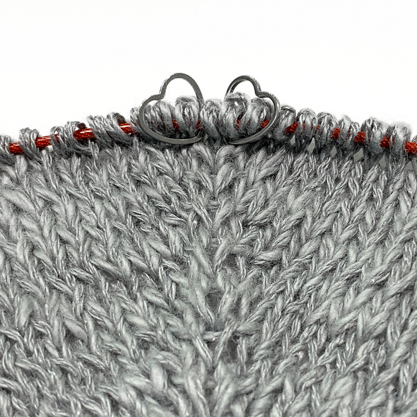 Two  small heart silver toned ring stitch markers on knitted swatch with grey yarn  by Pretty Warm Designs