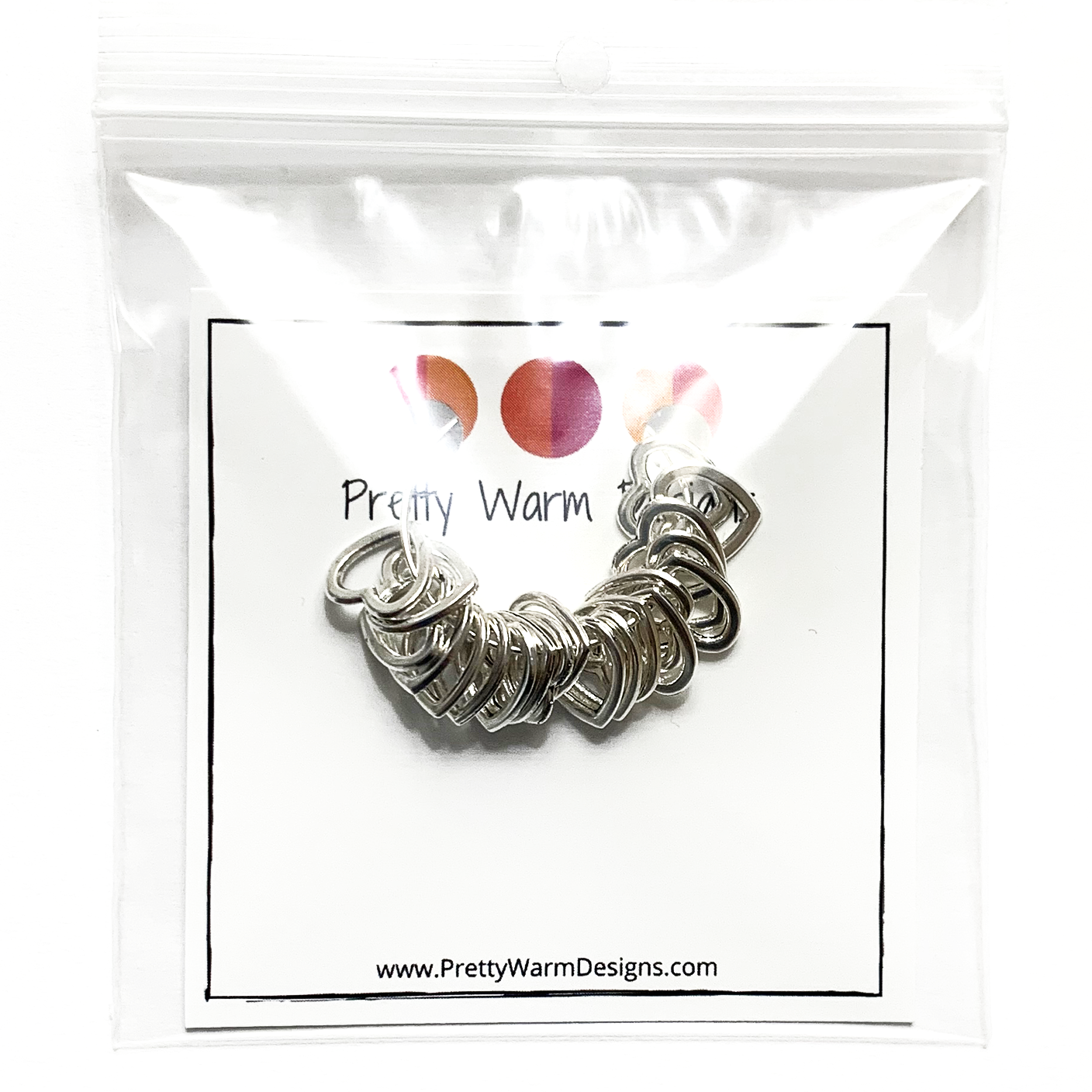 20 small heart stitch markers strung on a silver earring hoop attached to card stock with Pretty Warm Designs logo and text packaged in a clear poly bag