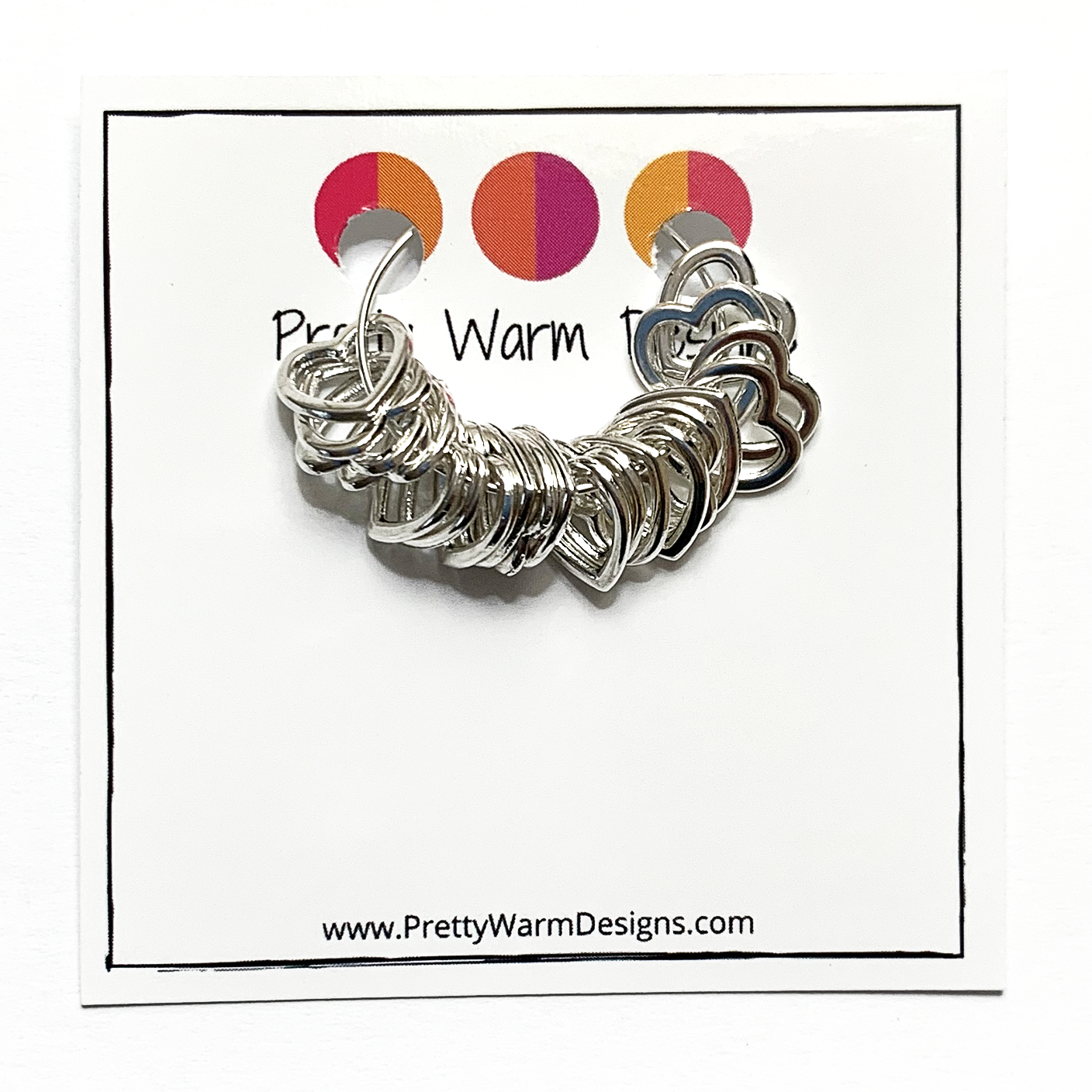 20 small heart stitch markers strung on a silver earring hoop attached to card stock with Pretty Warm Designs logo and text