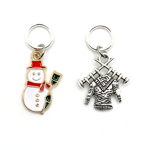 Two Winter-themed knitting ring stitch markers, one red, white and green enamel snowman and one antiqued Tibetan silver sweater on knitting needles