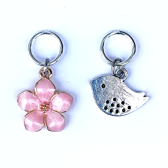 Two spring-themed knitting ring stitch markers, one pink enamel cherry blossom and one small silver song bird by Pretty Warm Designs