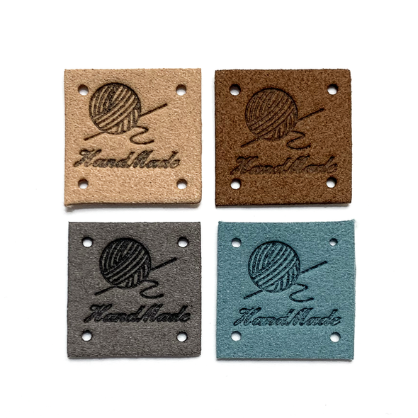 Four tan, brown, grey and teal square PU leather labels stamped with a ball of yarn graphic and Hand Made text sold by Pretty Warm Designs Inc.