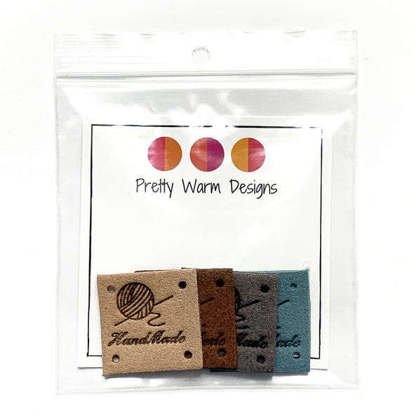 Four tan, brown, grey and teal square PU leather labels stamped with a ball of yarn graphic and Hand Made text sold by Pretty Warm Designs Inc. packaged in a clear poly bag