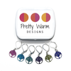 Six colour coated stainless steel round tree of life charm locking stitch markers for crochet and decorative storage tin with Pretty Warm Designs logo by Pretty Warm Designs Inc