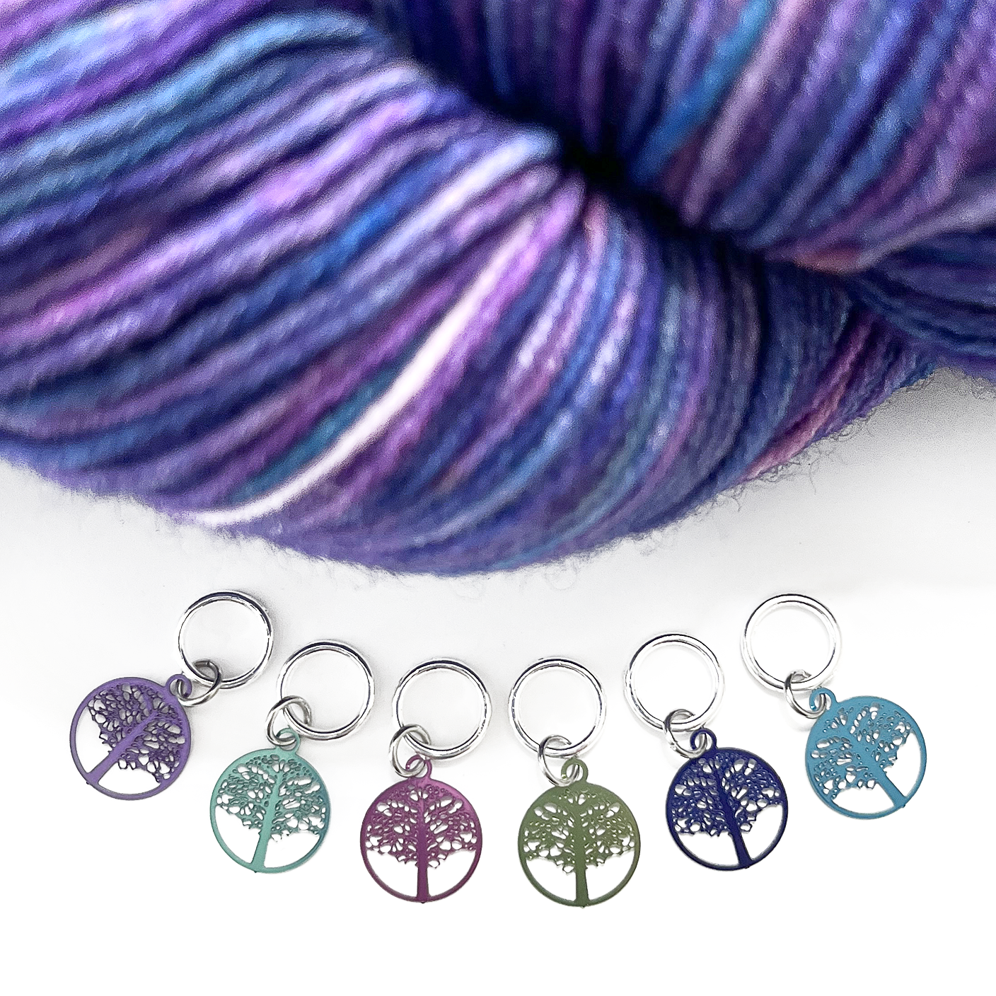 Six colour coated stainless steel round tree of life charm snag free ring stitch markers for knitting and purple variegated yarn by Pretty Warm Designs Inc