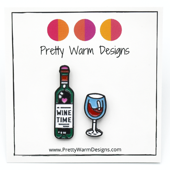 Set of two enamel pins, including bottle of wine enamel pin with Wine Time text on label and turquoise and red wine glass pin on white cardstock with Pretty Warm Designs text and logo
