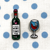 Set of two enamel pins, including bottle of wine enamel pin with Wine Time text on label and turquoise and red wine glass pin on blue polka dot fabric project bag