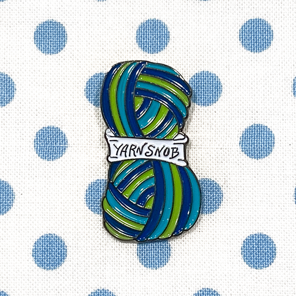 Blue, green and white enamel on silver metal Yarn Snob pin on a blue polka dot fabric project bag by Pretty Warm Designs